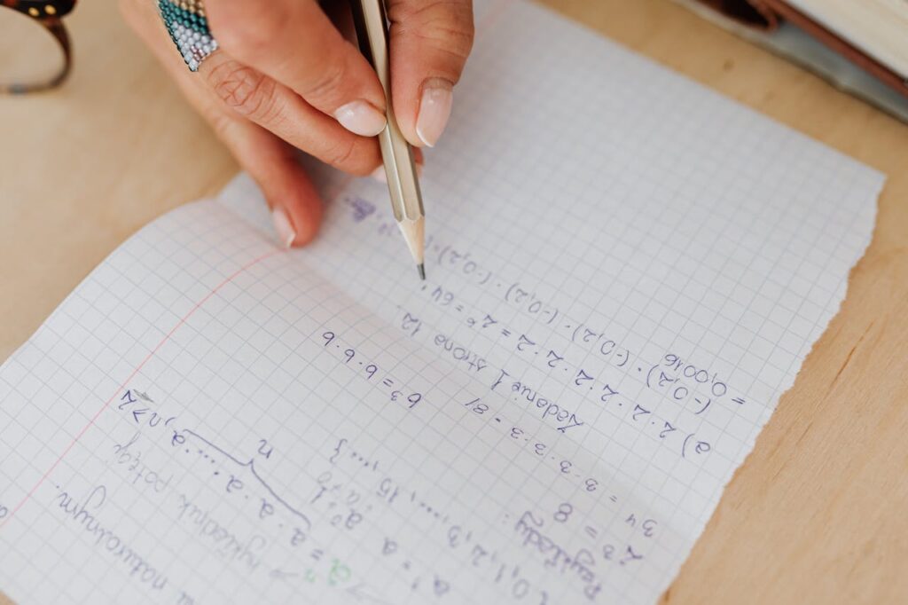 A person writes mathematical equations by hand on grid paper using a pencil, promoting learning.